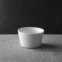 a white bowl sitting on top of a gray tablecloth next to a black wall