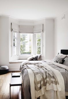 a bed sitting in a bedroom next to a window with white walls and wooden floors