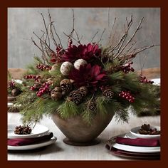 a vase filled with pine cones and red flowers on top of a table next to plates