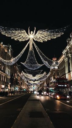 an angel statue is lit up in the night sky over a street lined with buildings