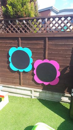 three flower cutouts are placed on the grass near a wooden fence with a blackboard attached to it