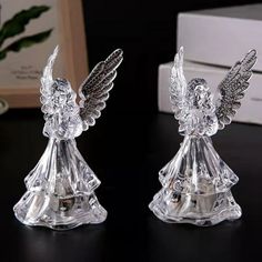 two clear glass angel figurines sitting on top of a black table next to a white box