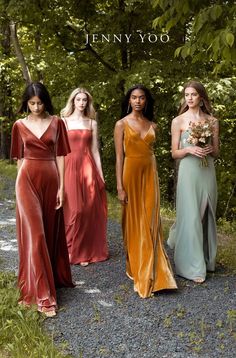 four women in long dresses standing on gravel path with trees in the backgroud