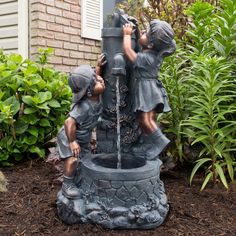 two children playing with a water fountain in front of a house and bushes on the side