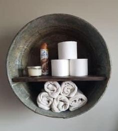 several rolls of toilet paper are stacked on a wooden shelf in a round bowl with two shelves holding rolled up towels