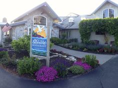 a sign in front of a building with flowers around it