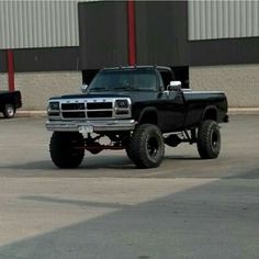 a black pickup truck parked in front of a building with large tires on it's flatbed