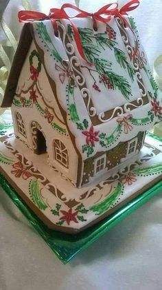 a gingerbread house decorated with holly and red bows on a green plate, sitting on a white tablecloth