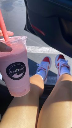 a person holding a pink drink in their hand while sitting on the back of a car