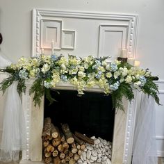 a fireplace decorated with white and blue flowers, greenery and logs for the mantel