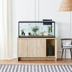 a fish tank sitting on top of a wooden cabinet next to a chair and lamp