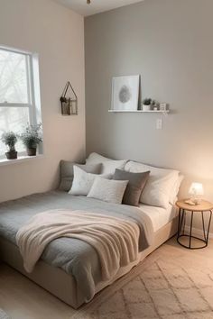 a bed sitting under a window next to a table with a lamp on top of it