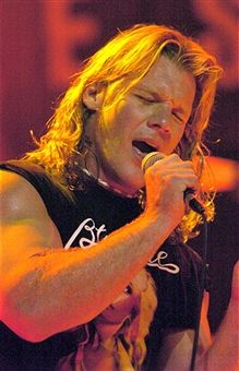 a man with long hair holding a microphone in his hand and singing into the microphone