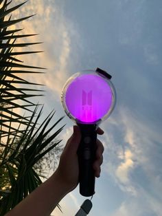 a hand holding a purple light in front of a palm tree and blue sky with clouds