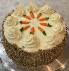 a cake with carrots on top is sitting on a platter and has frosting