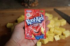 a hand holding a packet of kool - aid next to pineapples