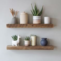 three wooden shelves with pots, candles and plants on them in front of a white wall