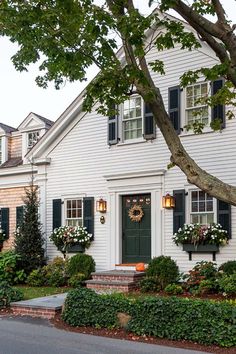 a white house with black shutters and wreaths on the front door is shown