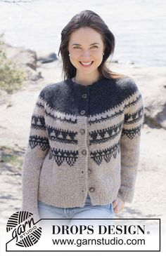 a woman standing on the beach wearing a cardigan sweater and smiling at the camera