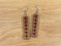 two wooden earrings with black crosses on them sitting on top of a wood table next to a pair of silver ear wires