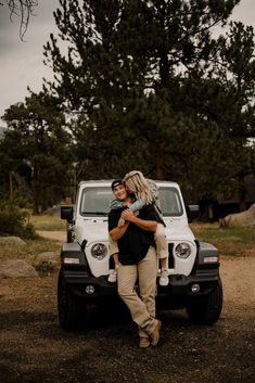 a man holding a woman in front of a white jeep