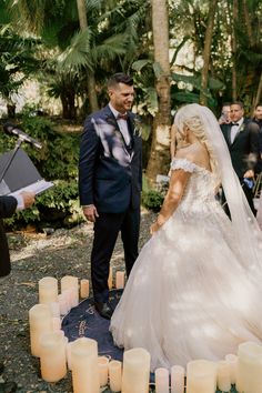 a bride and groom standing in front of candles at their outdoor wedding ceremony with guests looking on