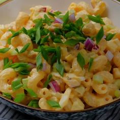 a bowl full of macaroni salad with onions and green garnish on top