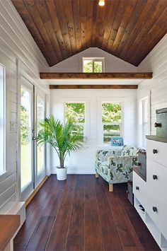 a living room with wooden floors and white walls, wood ceiling and large window above the couch