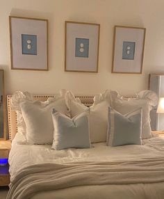 a bed with white linens and blue pillows in a bedroom next to two framed pictures on the wall