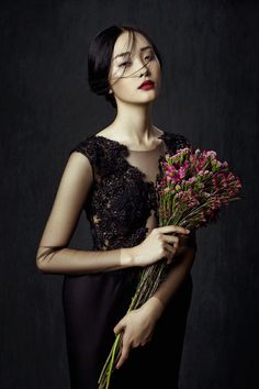 a woman in black dress holding flowers and posing for the camera with her eyes closed