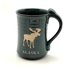 a green mug with a moose on the front and alaska written in gold lettering, against a white background