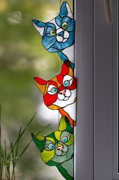 three colorful stained glass cats sitting on top of a window sill next to a potted plant