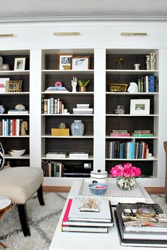 a living room filled with lots of books on top of a white table next to a book shelf