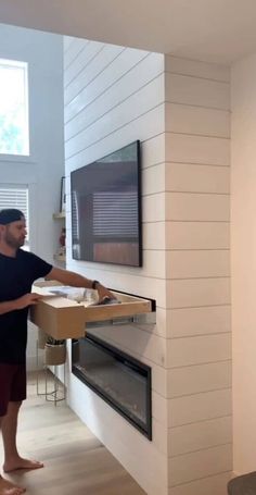 a man holding a box in front of a tv mounted on a wall above a fireplace