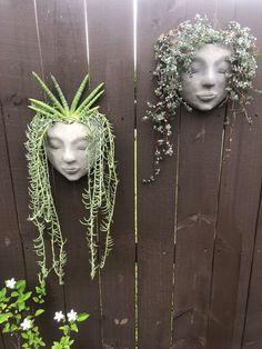 two masks with plants growing out of them on a fence next to a potted plant