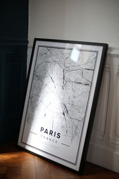 a black and white framed poster sitting on top of a wooden floor next to a wall