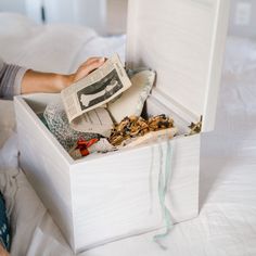 a person sitting on a bed with an open box filled with books and papers in it