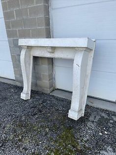 an old white marble fireplace mantel in front of a garage door with moss growing on the ground