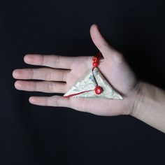 a person's hand holding a piece of white paper with red beads