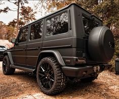 a black mercedes g - class is parked in the woods