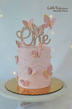 a pink cake decorated with butterflies and the number one on top is sitting on a plate