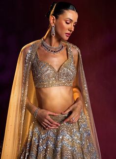 Embrace elegance with the Gold Sequins Embroidered Bridal Lehenga Set, a true masterpiece of craftsmanship and design. Crafted from soft net fabric, the golden lehenga boasts an intricately embroidered pattern, featuring a stunning blend of silver and gold sequins, crystals, and bugle beads that create a captivating sparkle from every angle. Teamed with a blouse equally adorned with detailed embroidery, this ensemble radiates luxury and sophistication. The look is completed with a sheer dupatta that adds an ethereal touch of elegance. This perfect blend of traditional artistry and modern style makes the ensemble ideal for making a memorable entrance. Perfect for a bride or bride-to-be, this lehenga set ensures you shine with grace and beauty on your special day. Composition : Lehenga, Blou Gold Embellished Choli, Embellished Gold Choli, Gold Embellished Lehenga For Reception, Gold Pre-draped Saree With Sheer Dupatta For Navratri, Festive Gold Embellished Choli, Glamorous Gold Sets With Intricate Embroidery, Gold Anarkali Pre-draped Saree With Sheer Dupatta, Glamorous Anarkali Set With Intricate Embroidery For Reception, Gold Pre-draped Saree With Intricate Embroidery For Reception