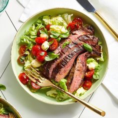 a salad with steak, lettuce and tomatoes in a bowl next to a fork