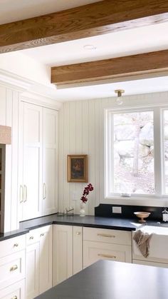 a kitchen with white cabinets and black counter tops in front of a large open window