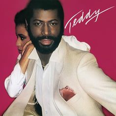 a man in a white suit and tie next to a woman with her hand on her ear