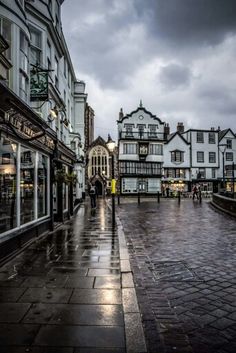 people are walking down the street in front of some buildings on a rainy day with dark clouds