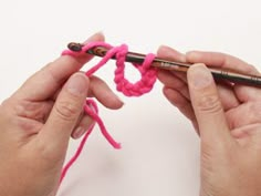 two hands crocheting the end of a piece of pink yarn