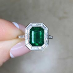 A halo engagement ring featuring a 2.66 carat emerald-cut natural green emerald. The emerald is bezel-set in platinum and surrounded by a halo of baguette cut diamonds with a total weight of 0.73 carats. Round brilliant cut diamonds weighing 0.14 carats total adorn the shoulders. The mounting is decorated with an openwork under-gallery and fine milgrain. This ring is handcrafted in platinum.
The measurements of this ring including the diamond halo are approximately 13.78mm x 12.18mm.
The current Luxury Octagon Emerald Ring With Diamond Accents, Luxury Emerald-cut Emerald Ring With Halo Design, Luxury Emerald Cut Emerald Ring With Halo Design, Emerald Cut Emerald Ring With Halo Setting, Emerald Ring With Halo Setting In Platinum, Green Emerald Ring With Halo Setting In Platinum, Platinum Baguette Cut Green Emerald Ring, Green Emerald Platinum Ring With Halo Setting, Octagon Emerald Ring With Halo Setting