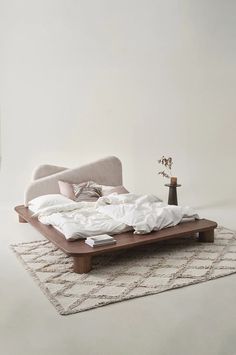 a bed sitting on top of a white rug next to a vase filled with flowers