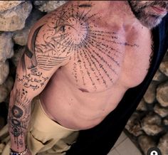 a man with lots of tattoos on his chest and arm is standing in front of some rocks